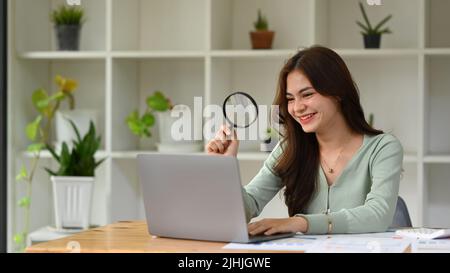 Femme Auditeur avec loupe pour vérifier le contenu en ligne sur un ordinateur portable Banque D'Images