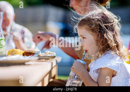 Repas de famille au barbecue dîner dans le jardin, petite fille de boire de l'eau et de l'apprécier. Banque D'Images