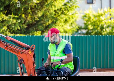Un homme sur une mini-pelle permet de nivrir un morceau de terre et de détacher le sol Banque D'Images