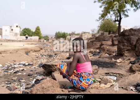 Jeune fille africaine assise sur la rive d'un lit de rivière érodé drainé rempli d'ordures et de grime; concept de réchauffement et de pollution de la planète Banque D'Images