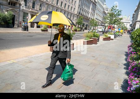 Un homme utilise un parapluie pour se protéger du soleil dans le centre de Londres, alors que les Britanniques sont sur le point de connaître la journée britannique la plus chaude jamais enregistrée alors que les températures devraient atteindre 40C. Date de la photo: Mardi 19 juillet 2022. Banque D'Images