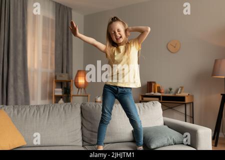 Bonne humeur petite fille dansant chantant debout sur le canapé à la maison Banque D'Images