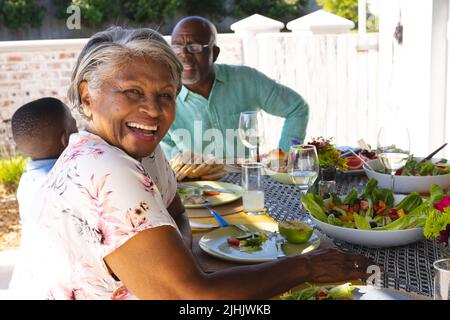 Portrait d'une femme âgée heureuse multiraciale prenant le petit déjeuner avec un homme âgé et un petit-fils à la maison Banque D'Images