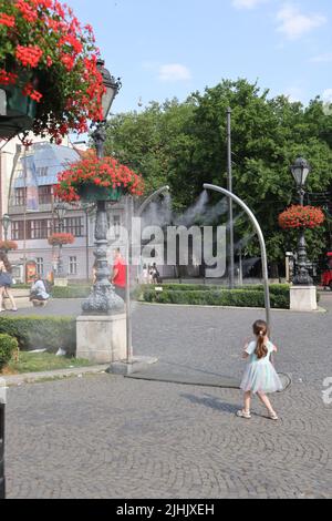 Les petites filles adorables aiment le refroidissement à partir de nébuliseurs publics sur une place de ville; le refroidissement par brouillard d'eau, le refroidissement par brouillard, les pulvérisateurs d'eau Banque D'Images