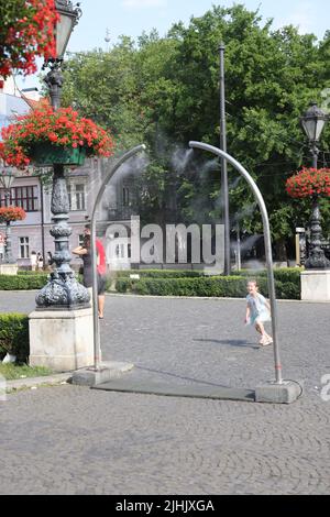 Les petites filles adorables aiment le refroidissement à partir de nébuliseurs publics sur une place de ville; le refroidissement par brouillard d'eau, le refroidissement par brouillard, les pulvérisateurs d'eau Banque D'Images