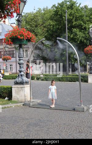 Les petites filles adorables aiment le refroidissement à partir de nébuliseurs publics sur une place de ville; le refroidissement par brouillard d'eau, le refroidissement par brouillard, les pulvérisateurs d'eau Banque D'Images