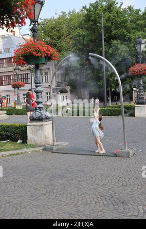 Les petites filles adorables aiment le refroidissement à partir de nébuliseurs publics sur une place de ville; le refroidissement par brouillard d'eau, le refroidissement par brouillard, les pulvérisateurs d'eau Banque D'Images