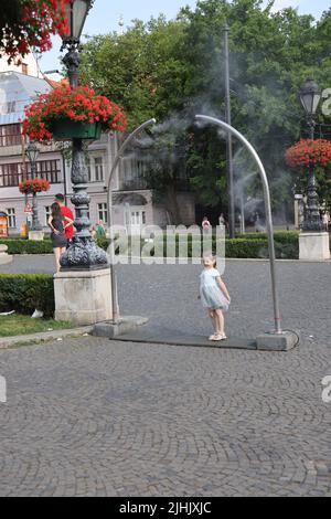 Les petites filles adorables aiment le refroidissement à partir de nébuliseurs publics sur une place de ville; le refroidissement par brouillard d'eau, le refroidissement par brouillard, les pulvérisateurs d'eau Banque D'Images