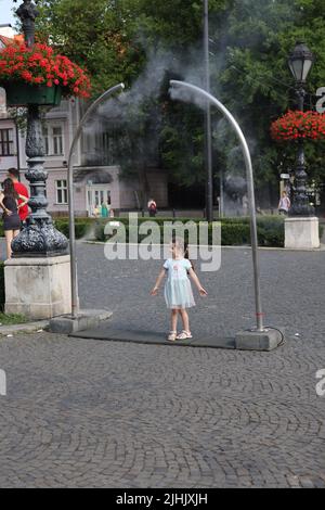 Les petites filles adorables aiment le refroidissement à partir de nébuliseurs publics sur une place de ville; le refroidissement par brouillard d'eau, le refroidissement par brouillard, les pulvérisateurs d'eau Banque D'Images