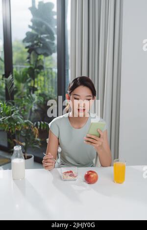 une femme asiatique mange un déjeuner avec son téléphone entre ses mains Banque D'Images