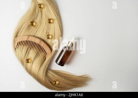 Une huile ou un sérum naturel essentiel pour les soins des cheveux dans des capsules dorées sur un brin de cheveux blonds. Concept de soins et de lissage des cheveux Banque D'Images