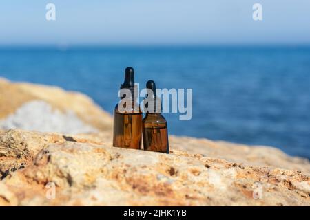 Huiles essentielles naturelles ou sérum en flacons compte-gouttes bruns, debout sur les pierres du bord de mer Banque D'Images