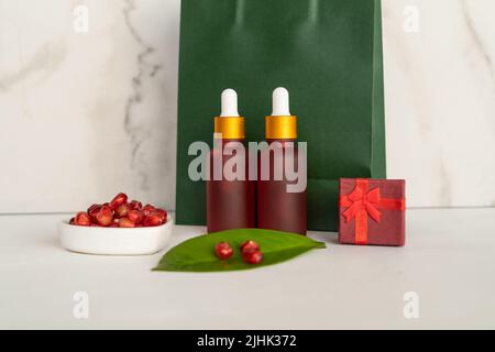 Flacons compte-gouttes rouges de sérum ou d'huile de grenade sur un sac de shopping en papier vert comme cadeau pour les vacances Banque D'Images
