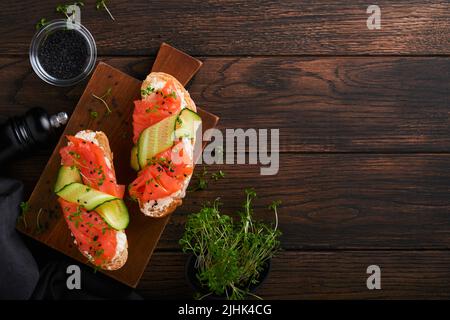 Sandwichs. Toast au saumon avec fromage à la crème, concombre, sésame noir et microverts sur fond de table en bois. Fruits de mer. Une alimentation saine. Photographie Banque D'Images