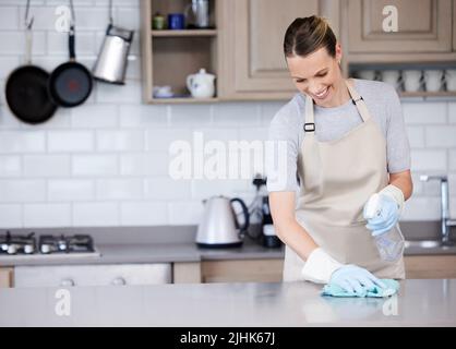 Les surfaces brillantes sont si satisfaisantes. Une jeune femme essuyant une surface de cuisine avec un détergent et un chiffon à la maison. Banque D'Images