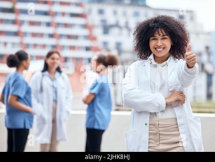 Portrait d'un jeune heureux médecin mixte de course en faisant un geste avec ses collègues en arrière-plan. Groupe de médecins et d'infirmières travaillant en collaboration Banque D'Images