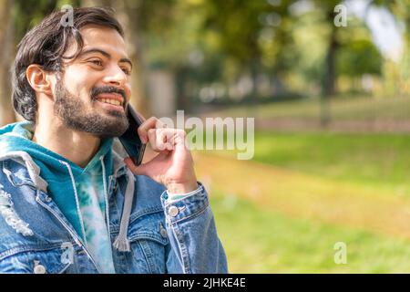 Jeune latino parlant au téléphone cellulaire dans un parc Banque D'Images