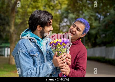 Couple de Latino gay hommes dans un parc s'embrassant. L'un surprend l'autre avec un bouquet de fleurs comme cadeau Banque D'Images