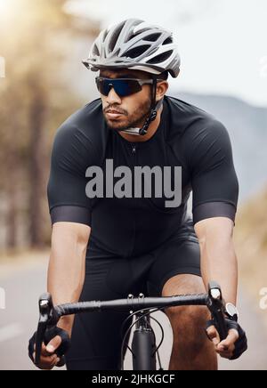 Homme indien en forme et actif portant un casque et des lunettes de soleil pour faire du vélo à l'extérieur pour un entraînement. Athlète de course mixte concentré s'exerçant avec un vélo Banque D'Images