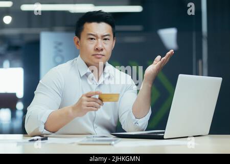 Portrait d'un homme d'affaires frustré et en colère, homme travaillant au bureau, tenant une carte de crédit et regardant l'appareil photo, inquiet au sujet de la limite de crédit et contrarié Banque D'Images