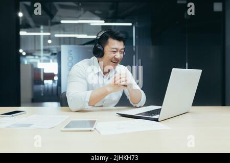 Un homme d'affaires asiatique heureux regardant un match sportif en ligne, un homme au bureau regardant l'écran d'un ordinateur portable applaudisse Banque D'Images