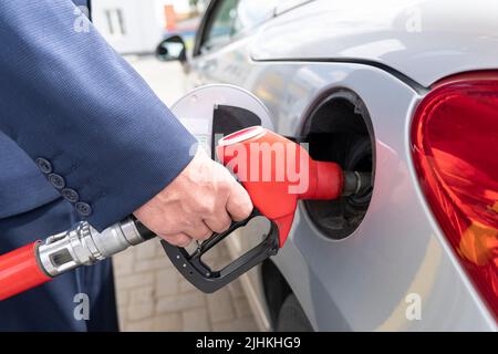 homme d'affaires en costume gère sa voiture avec de l'essence dans une station-service. Gros plan sur les pistolets à carburant à main et rouge. Banque D'Images