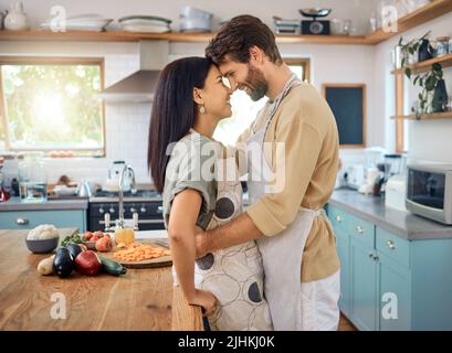 Couple interracial heureux touchant les fronts tout en partageant un moment intime romantique à la maison tout en portant des tabliers et en cuisinant ensemble. Jeune caucasien Banque D'Images