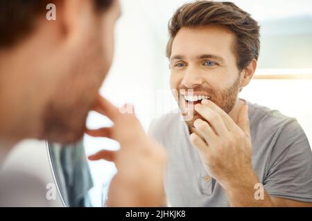 Un bel homme qui vérifie ses dents dans une salle de bains à la maison. Homme caucasien nettoyant ses dents et regardant dans un miroir dans son appartement. Banque D'Images