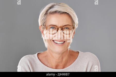 Portrait d'une belle femme mature caucasienne isolée contre un fond gris de studio portant des lunettes. Femme âgée souriant et la montrant Banque D'Images