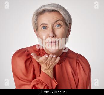 Une heureuse femme de race blanche mûre soufflant un baiser avec ses mains sur un fond gris. Femme vieillissante utilisant le langage corporel pour exprimer l'amour, la bonté Banque D'Images
