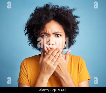 C'est choquant. Une jeune femme attrayante debout seule sur fond bleu dans le studio et a l'air choqué. Banque D'Images