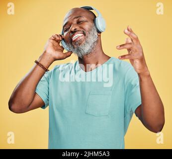 Un heureux homme afro-américain mature portant des écouteurs et écoutant de la musique tout en dansant sur fond jaune dans le studio. Noir souriant Banque D'Images