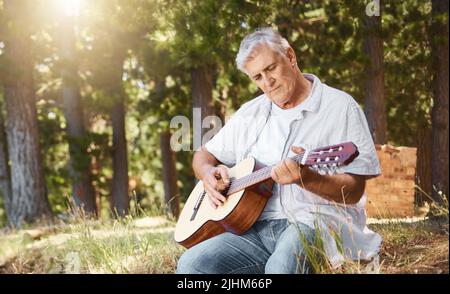 Un beau homme mature jouant de la guitare en campant dans les bois. Banque D'Images