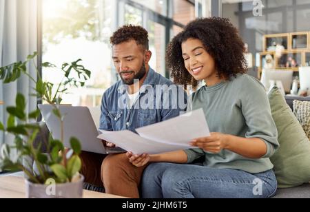 Jeune couple de course mixte heureux passant par des documents et utilisant un ordinateur portable à une table ensemble à la maison. Mari et femme hispaniques planifiant et payant Banque D'Images