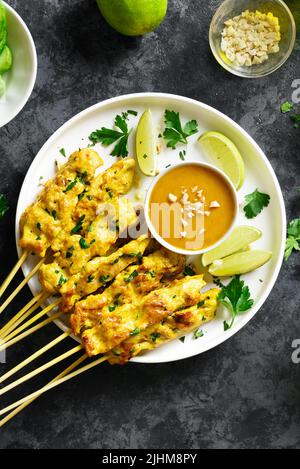 Brochettes de poulet grillées servies avec une sauce trempée aux arachides sur une assiette sur fond de pierre sombre. Vue de dessus, plan d'appartement Banque D'Images