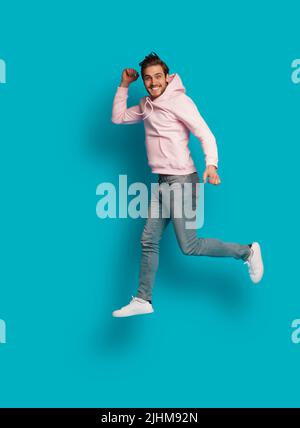 Photo pleine grandeur de jeune heureux excité souriant positif homme sautant isolé sur fond bleu clair de couleur Banque D'Images