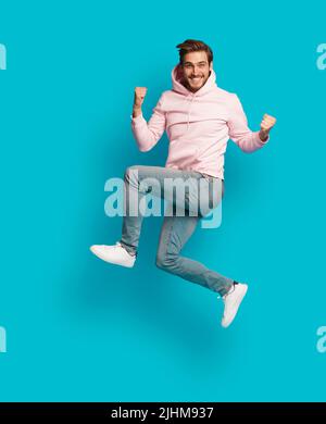Photo pleine grandeur de jeune heureux excité souriant positif homme sautant isolé sur fond bleu clair de couleur Banque D'Images