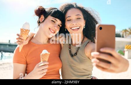Selfies et crèmes glacées. Deux jeunes filles attrayantes prenant des selfies tout en appréciant des glaces sur la plage. Banque D'Images