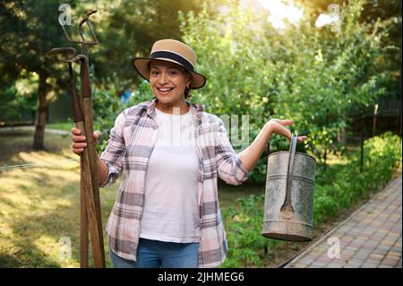 Belle femme, ouvrier agricole avec des outils de jardin dans ses mains aime le jardinage sur une belle journée ensoleillée d'été. Agriculture écologique, jardinage, culture biologique Banque D'Images