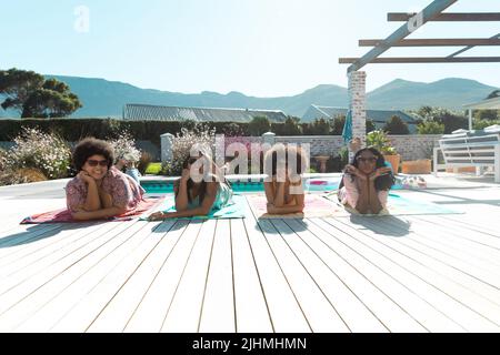 Jeunes filles biraciales stylées portant des lunettes de soleil et posant au bord de la piscine en été Banque D'Images
