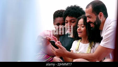 Les parents interraciaux et les enfants ethniquement divers rient au contenu des médias sociaux sur leur téléphone portable Banque D'Images