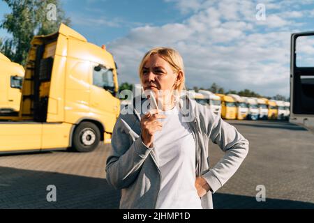 Femme originaire du Caucase d'âge moyen travaillant comme conducteur de camion. Fumer sur un parking de camions Banque D'Images