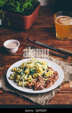 Steak de porc et pâtes crémeuses aux épinards et au thym Garni de parmesan râpé sur plaque blanche Banque D'Images