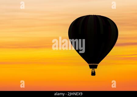 Un ballon d'air chaud est silhoueté contre le ciel au coucher du soleil dans une image composite. Banque D'Images