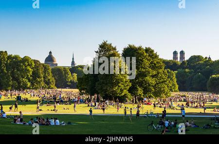 Munich, Allemagne. 19th juillet 2022. Les gens apprécient les rayons chauds du soleil sur la grande pelouse du jardin anglais le soir. En arrière-plan, on peut voir le dôme de la Chancellerie d'Etat (l-r), le Vieux Pierre et les deux tours de la Frauenkirche. Credit: Peter Kneffel/dpa/Alay Live News Banque D'Images