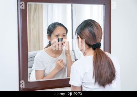 Belle femme asiatique regardant le miroir, appliquant le masque charbon de bois nettoyage profond nez bande de pore sur la peau propre fraîche. Soins de beauté et de soin de la peau Banque D'Images