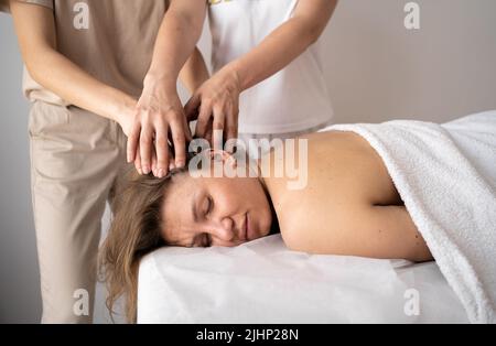 Belle jeune femme couché avec les yeux fermés et ayant un massage de la tête au spa en quatre mains. Massage étudiant de masseur formation. Beauté, style de vie et rel Banque D'Images