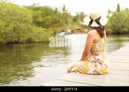 Jeune femme regardant s'asseoir au quai avec chapeau et robe à bocas del toro panama Banque D'Images