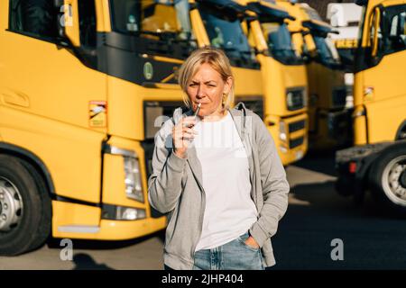 Femme originaire du Caucase d'âge moyen travaillant comme conducteur de camion. Fumer sur un parking de camions Banque D'Images