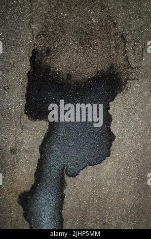 Une flaque et des taches humides sur l'asphalte sous la forme de la tête d'un homme noir avec une grande coupe de cheveux légère. Banque D'Images